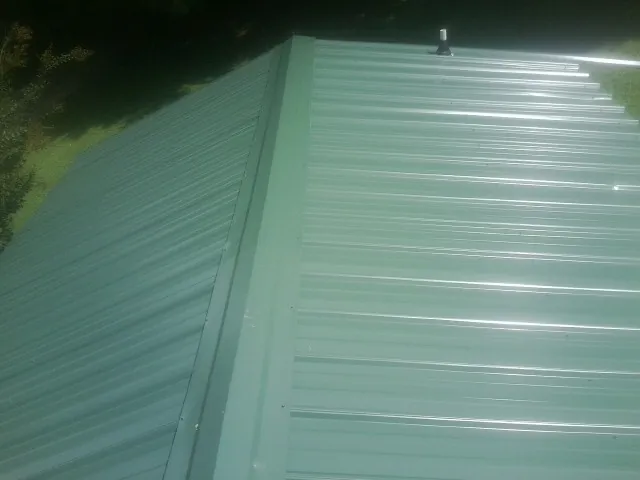 New green metal panels meeting at the ridge of a roof — Flat Roof Repair work by our crew in Victor